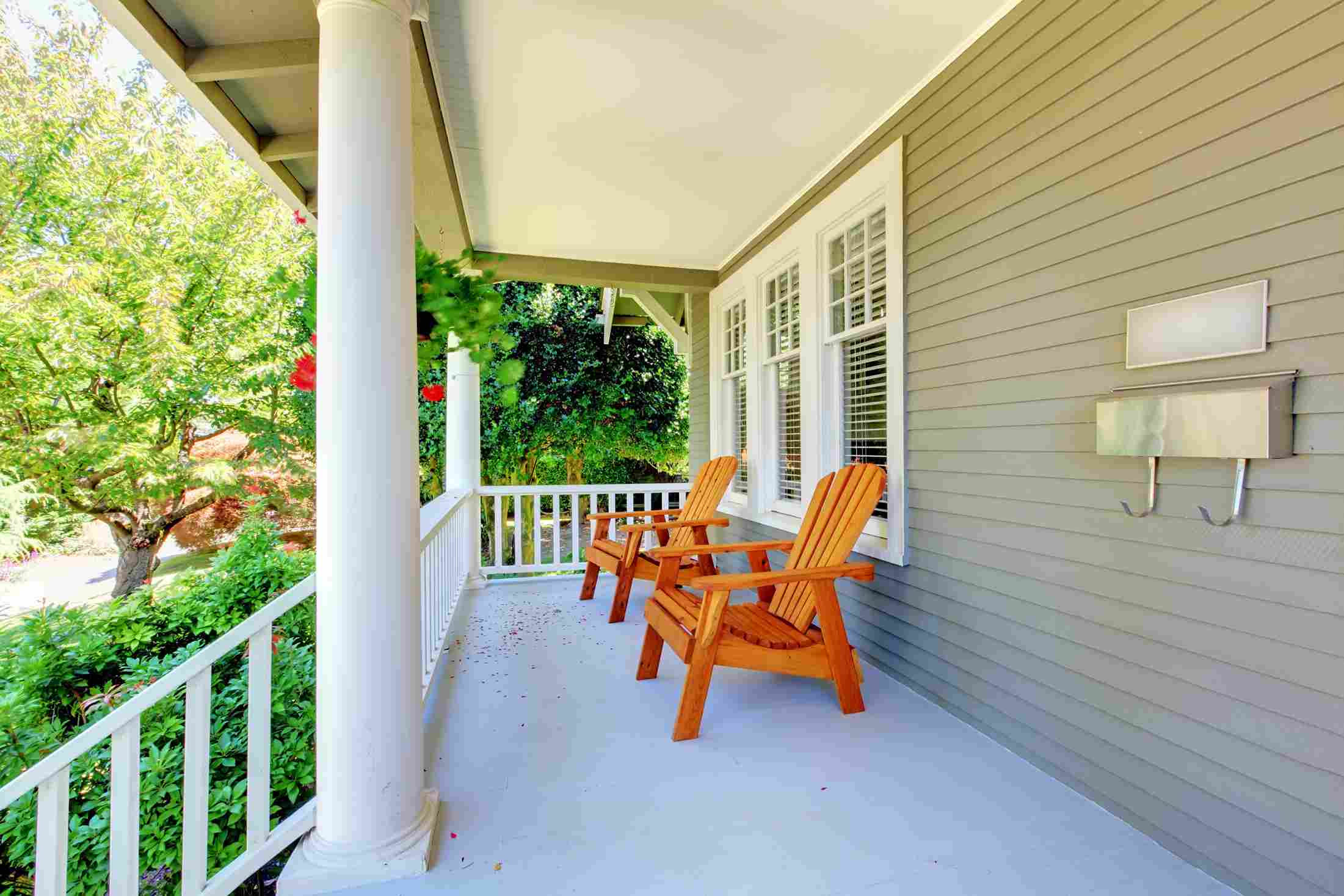 Cozy front porch with wooden chairs, white railing, lush greenery, and red flowers in Raleigh, NC