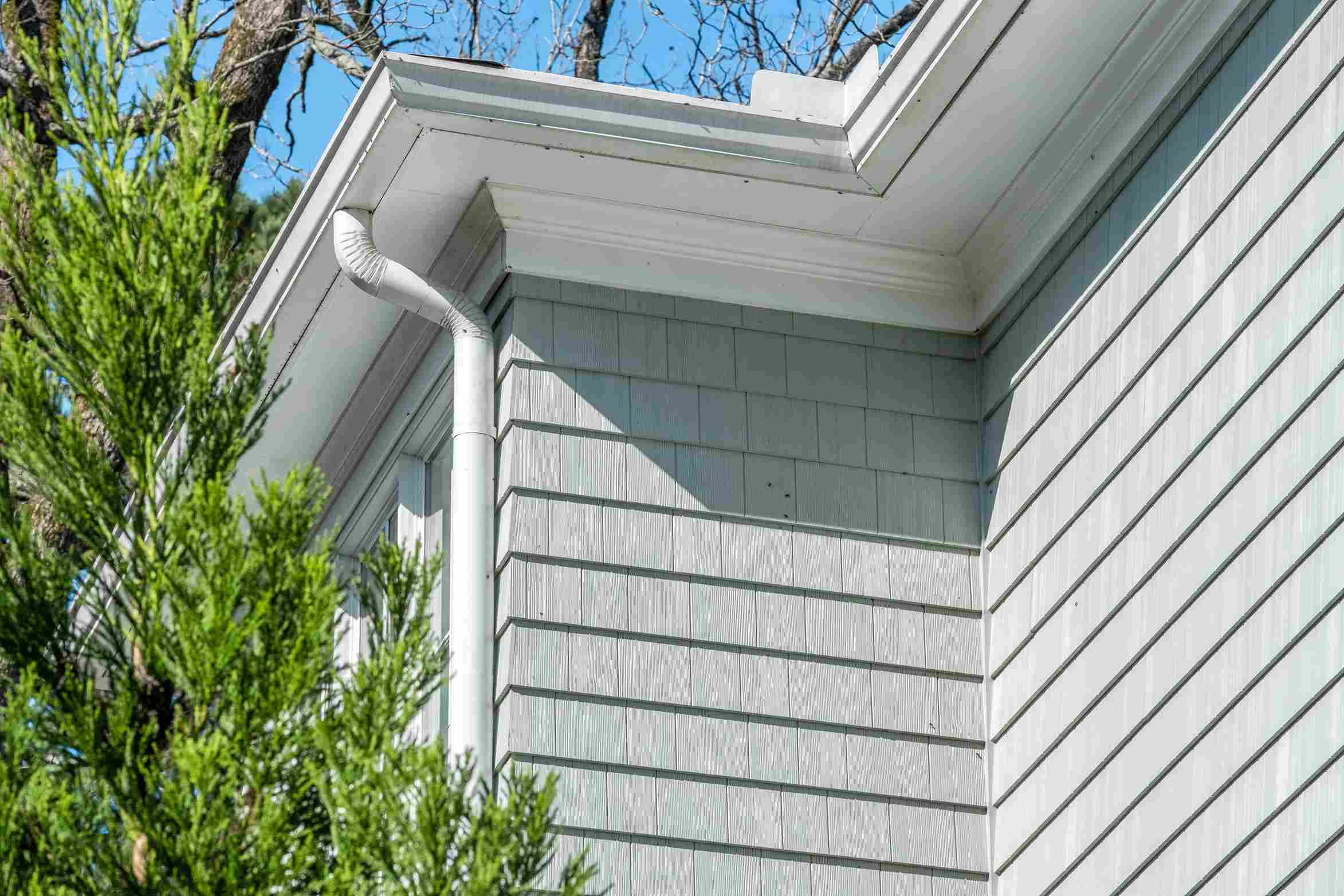Light gray house exterior with white gutters, green foliage, and clear blue sky in Raleigh, NC