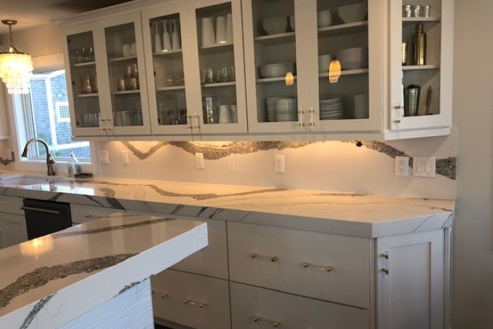Modern kitchen with glass-front cabinets, marble countertops, and under cabinet lighting