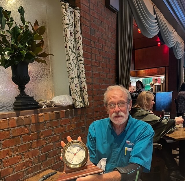 Dave Purvis holding commemorative clock at restaurant during 50-year work anniversary celebration