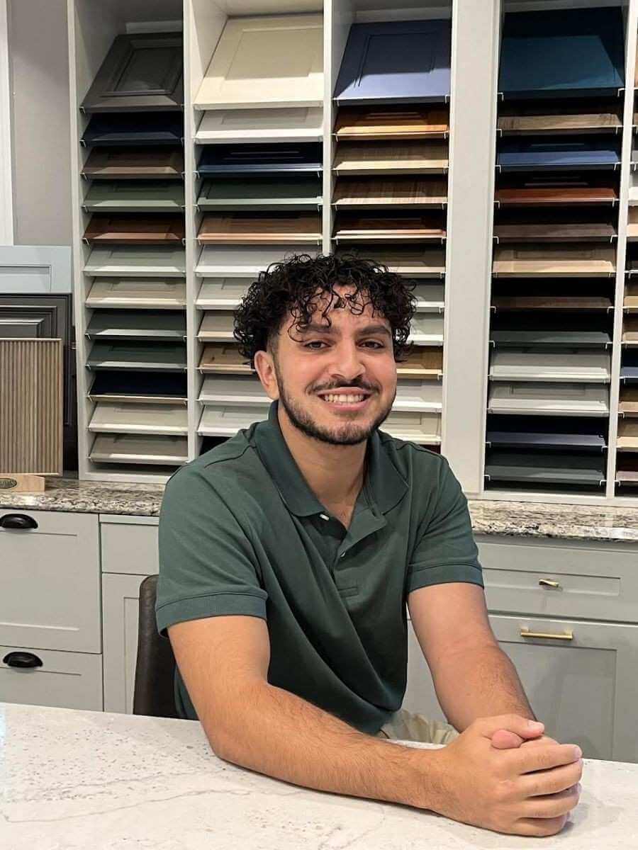 Karim Mohamed designer seated at showroom counter with cabinet samples and finishes display behind