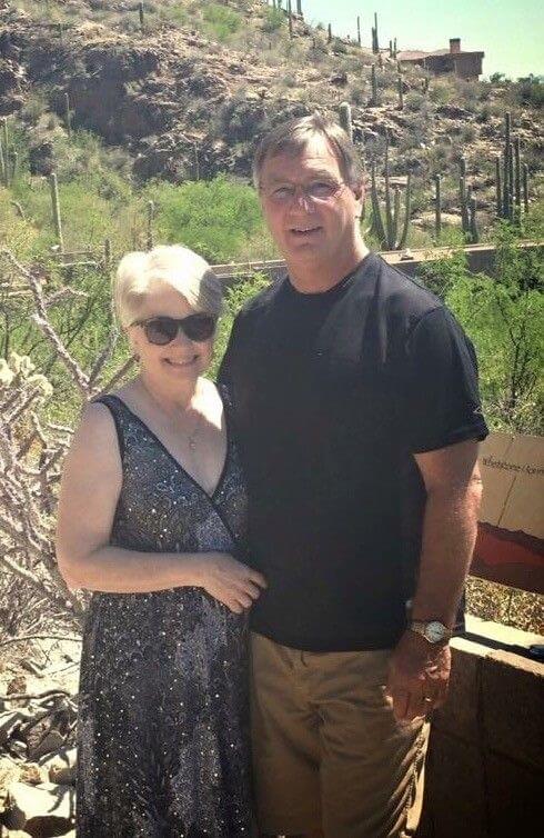 Mike and Julie standing outdoors in desert landscape with cacti and scenic mountain backdrop