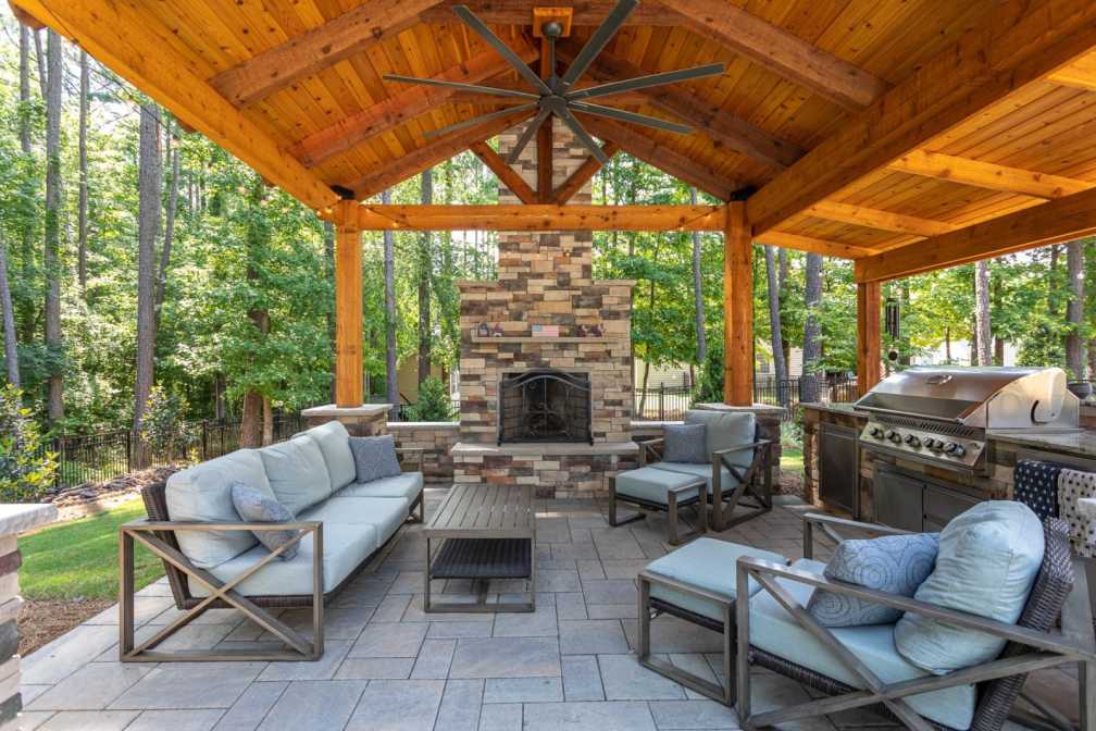 Rustic outdoor pavilion featuring a stone fireplace and a gabled wooden ceiling
