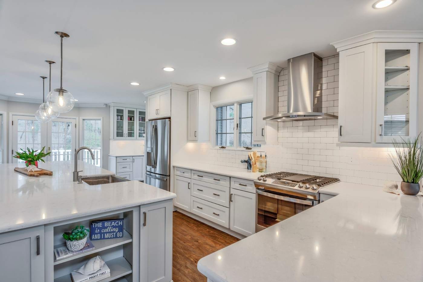Bright white kitchen with quartz countertops, island sink, subway tile, and stainless appliances