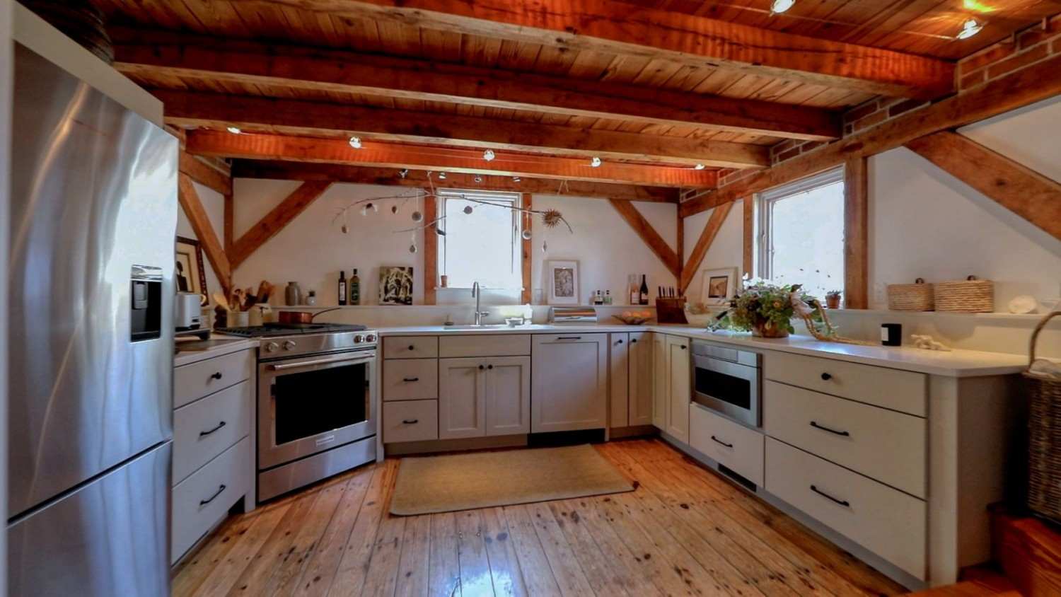 Rustic kitchen with exposed wood beams, white cabinetry, stainless appliances, and warm lighting
