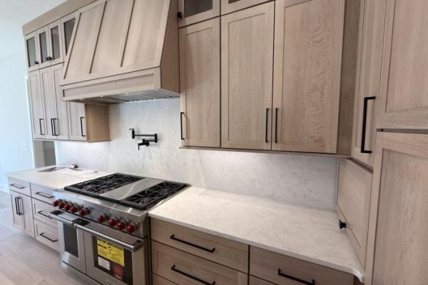 Modern light wood kitchen cabinets with black handles and marble backsplash